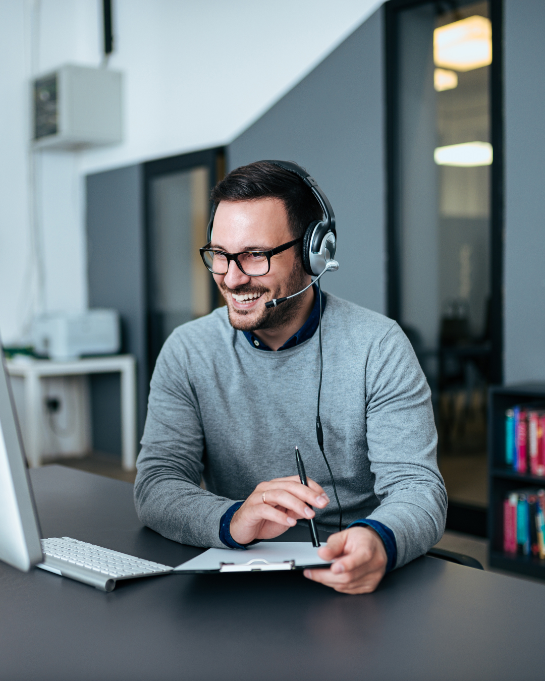 Man wearing head set smiling at computer work in help center
